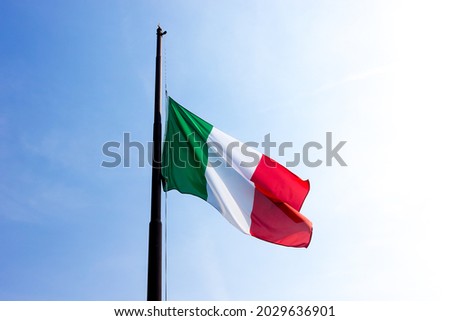italian flag flying at half-mast against a blue sky 