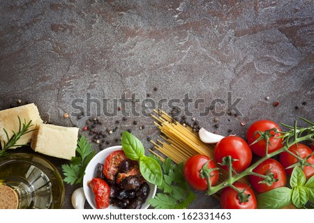 Italian food background, with vine tomatoes, basil, spaghetti, mushrooms, olives, parmesan, olive oil, garlic, peppercorns, rosemary, parsley and thyme.  Slate background.