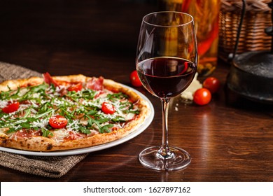 Italian food. Classic thin pizza with large sides, prosciutto, cherry tomatoes, arugula, parmesan cheese. Serving dishes in a restaurant on a white plate with red wine. - Powered by Shutterstock