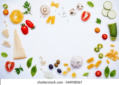 Italian food concept .Various kind of pasta with ingredients sweet basil ,tomato ,garlic ,parsley ,bay leaves ,pepper ,champignon,zucchini and parmesan cheese on white wooden background flat lay. - Shutterstock ID 544938367