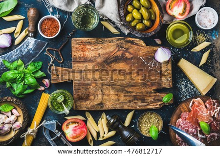 Italian food cooking ingredients on dark background with rustic wooden chopping board in center, top view, copy space