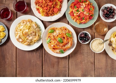 Italian Food And Drinks. Various Pastas, Olives, Wine, Grated Parmesan Cheese, Overhead Flat Lay Shot On A Rustic Background With Copy Space