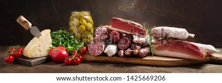 Italian food. Various kind types of salami, speck, sausages, parmesan cheese, green olives, basil and fresh tomatoes on a wooden table