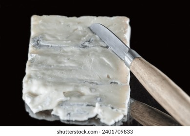 Italian Gorgonzola cheese on a black background with mirror effect and a cheese knife with a wooden handle resting on it, different layers of blue and cream visible - Powered by Shutterstock