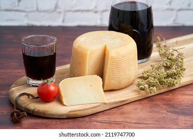 Italian hard cheese such as pecorino or caprino, wine in carafe and a bunch of oregano with sliced cheese on a wooden board. Traditional Italian wine glass and tomato.                            