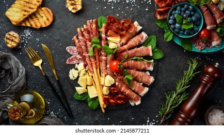 Italian ingredients: ham, prosciutto, salami, parmesan, olives, bread sticks. On a black stone background. - Shutterstock ID 2145877211