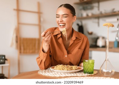 Italian inspiration. Happy young european woman enjoying freshly cooked pasta, holding fork and smiling, sitting in cozy kitchen interior, free space - Powered by Shutterstock