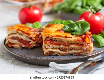 Italian lasagna with tomato sauce and cheese served with tomatoes and spinach, light concrete background. Homemade vegetarian lasagna. Selective focus.