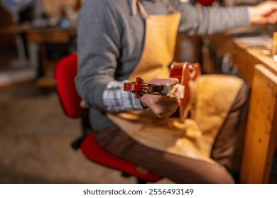 Italian luthier meticulously checks the scroll and pegbox of a handcrafted violin, showcasing the artistry and precision of traditional violin making - Powered by Shutterstock