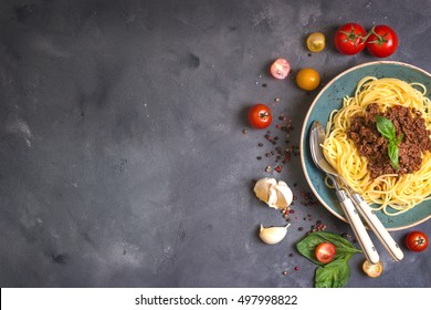 Italian Pasta Bolognese. Spaghetti With Meat And Tomato Sauce In A Plate On A Rustic Concrete Background. With Fresh Cherry Tomatoes, Basil, Garlic. Ingredients For Cooking. Space For Text. Top View