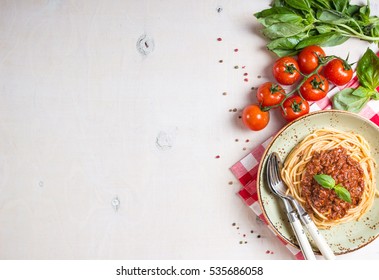 Italian Pasta Bolognese. Spaghetti With Meat And Tomato Sauce In A Plate With Italian Tablecloth On A Wooden White Background. With Fresh Cherry Tomatoes, Basil. Food Frame. Space For Text. Top View