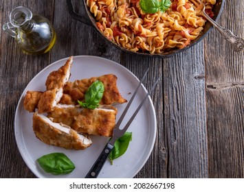 Italian Pasta Dish With Breaded Chicken Served With Fusilli In A Delicious Tomato, Basil Sauce On Wooden Table. Overhead View