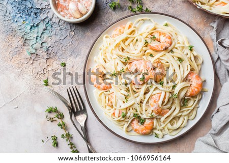 Italian pasta fettuccine in a creamy sauce with shrimp on a plate, top view