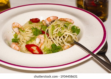 Italian Pasta. On A Plate Of Spaghetti With Shrimp, Spinach And Pepper, Someone Is Eating Pasta With A Fork. The Olive Oil Bottle Is Blurred In The Background. Mediterranean Diet Food.