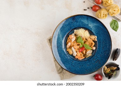 Italian Pasta With Seafood And Fresh Basil On A Blue Plate With A Napkin On A Light Background. Top View With A Copy Space For The Text. Food From The Restaurant. Horizontal Orientation.