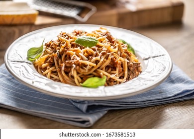 Italian pasta spaghetti bolognese served on white plate with parmesan cheese and basil.