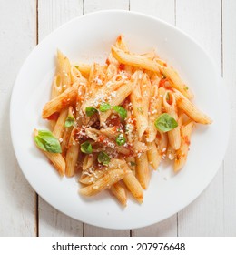 Italian Penne Pasta Or Noodles With A Savory Tomato Sauce, Fresh Basil And Grated Parmesan Cheese Viewed Close Up From Above On A White Plate In Square Format