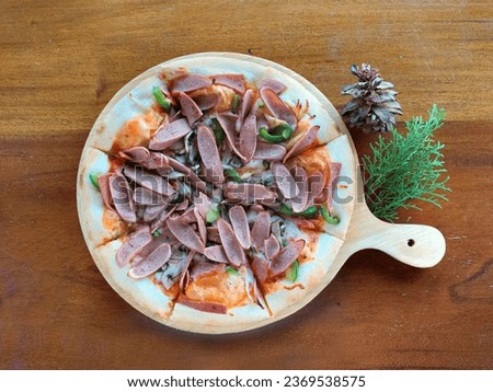 Italian pizza with cheese crest, Bolognese paste, paprika or bell pepper, cut pork sausages and herbs, with some pine nuts accessories on a wooden table background. On a white mozaic tiles table.