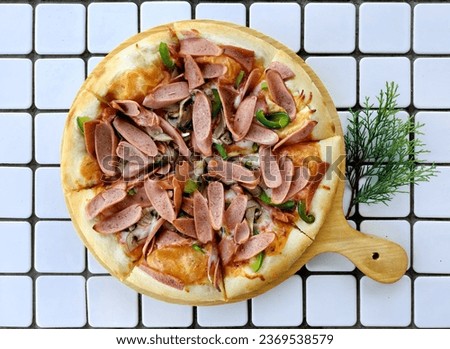 Italian pizza with cheese crest, Bolognese paste, paprika or bell pepper, cut pork sausages and herbs, with some pine nuts accessories on a wooden table background. On a white mozaic tiles table.