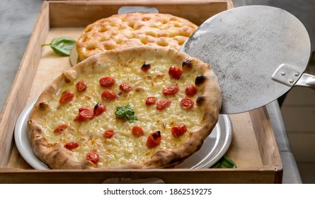 Italian pizza with cherry tomatoes and mozzarella cheese, detail of the oven shovel that unloads the freshly baked pizza on wooden tray