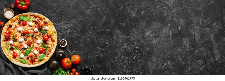 Italian pizza and pizza cooking ingredients on black concrete background. Tomatoes on vine, mozzarella, black olives, herbs and spices. Copy space for text. Banner composition - Shutterstock ID 1183461973