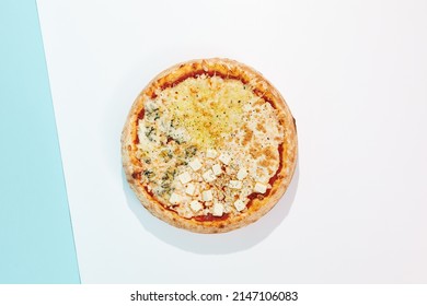 Italian pizza with four cheese on coloured background. Quattro formaggi pizza in minimal style on blue and orange color. American pizza delivery concept with color backdrop.