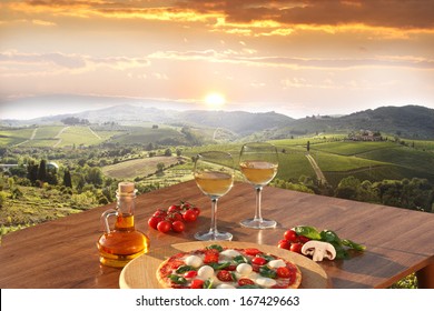 Italian pizza and glasses of white wine in Chianti, famous vineyard landscape in Italy