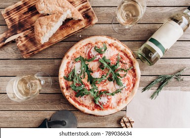 Italian pizza margherita with arugula, with a bottle and two glasses of white wine on a wooden table