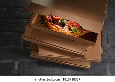 Italian Pizza Packed Ready To Go In A Brown Cardboard Takeout Box On Top Of A Stacked Order On Black Tiles