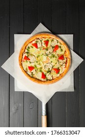 Italian pizza with zucchini, bell pepper, eggplant, cheese and pesto sauce on wooden background. Delicious hot pizza on baking shovel just from oven. Uncut vegetarian pizza on parchment paper