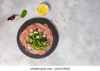 Italian Popular Meat Appetizer Carapaccio, Made Of Thin Slices Of Beef Tenderloin Or Turkey Fillet. Top View On A Gray Background With Lemon And Lettuce Leaves, A Copy Of The Space.