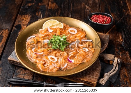 Italian Salmon carpaccio with onion and arugula served on a plate. Wooden background. Top view.