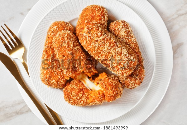 Italian snack suppli al telefono or rice\
croquettes stuffed with mozzarella cheese served on a white plate\
on a light marble background, top view,\
close-up