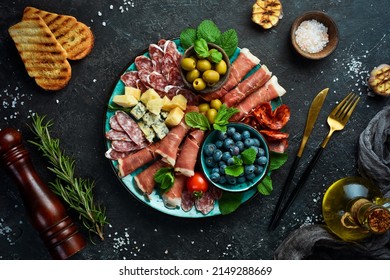 Italian snacks. Plate with cheese and ham, prosciutto, jamon salami, and snacks. On a black stone background. - Shutterstock ID 2149288669