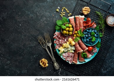 Italian snacks. Plate with cheese and ham, prosciutto, jamon salami, and snacks. On a black stone background. - Shutterstock ID 2161626471