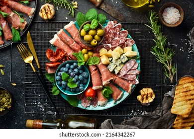 Italian snacks. Plate with cheese and ham, prosciutto, jamon salami, and snacks. On a black stone background. - Shutterstock ID 2164342267