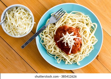 Italian Spaghetti Bolognese Garnished With Grated Gruyere Cheese With A Side Dish Containing Additional Cheese Alongside, Overhead View On A Wooden Table