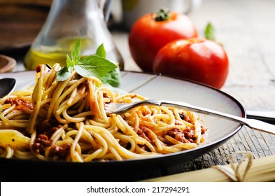 Italian spaghetti on rustic wooden table. Mediterranean cuisine with pasta ingredients- bolognese sauce, olive oil, basil and tomato.