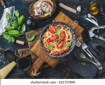 Italian Style Pasta Dinner. Spaghetti With Tomato And Basil In Plate On Wooden Board And Ingredients For Cooking Pasta Over Dark Plywood Background, Top View