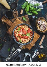 Italian Style Pasta Dinner. Spaghetti With Tomato And Basil In Plate On Wooden Board And Ingredients For Cooking Pasta Over Dark Blue Wooden Background, Top View