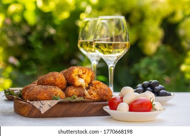 Italian summer aperitif. White wine glasses and snacks: Supplì - italian deep-fried snacks consisting of rise filled with mozzarella, black olives, mozzarella cheese, tomatoes. - Powered by Shutterstock