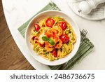 Italian summer seafood pasta directly above. Prawn, tomato and courgette, or zucchini, spaghetti in a white plate on a round marble table.