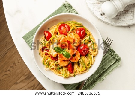 Italian summer seafood pasta directly above. Prawn, tomato and courgette, or zucchini, spaghetti in a white plate on a round marble table.