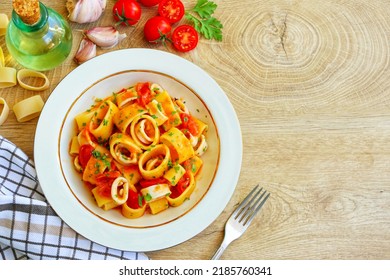 Italian Traditional Dish"Calamarata con calamari",calamarata pasta with squid,cherry tomatoes,olive oil,garlics,white wine,salt,pepper and parleys on plate with wooden background.Top view.Copy space - Shutterstock ID 2185760341