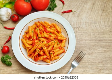 Italian Traditional Dish"Penne all'arrabbiata"or "Spicy penne pasta",penne pasta with tomato sauce,chilli pepper,garlic,olive oil,salt and parleys on plate with wooden table background.Copy space - Shutterstock ID 2050622303