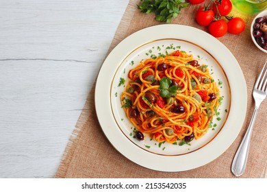 Italian Traditional Dish"Spaghetti alla Puttanesca",spaghetti with tomato sauce,anchovy,capers,olives,olive oil,peppers and parleys on plate with white wood table background.Top view.Copy space - Shutterstock ID 2153542035
