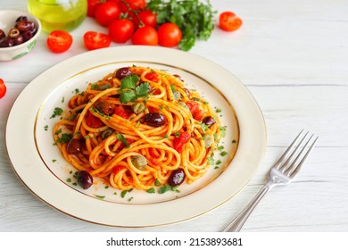 Italian Traditional Dish"Spaghetti alla Puttanesca",spaghetti with tomato sauce,anchovy,capers,olives,olive oil,peppers and parleys on plate with white wood table background.Simple and easy recipe
 - Shutterstock ID 2153893681