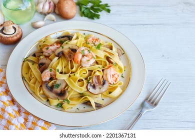 Italian Traditional Dish"Tagliatelle con Funghi e Gamberi",tagliatelle pasta with mushrooms,prawns,olive oil,garlics,parleys,salt and peppers on plate with white wood background.Copy space - Shutterstock ID 2201367131