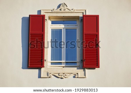 Italian window on the bright white wall facade with open red color classic shutters