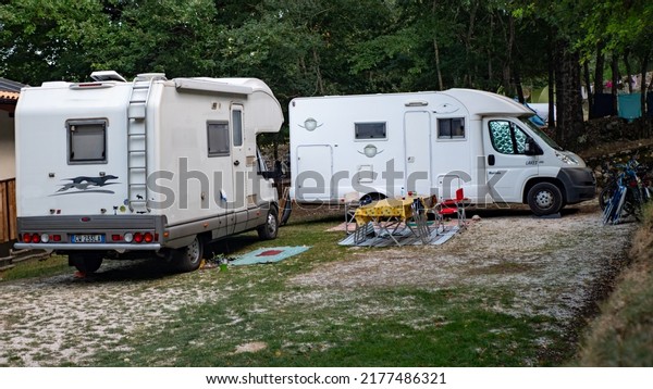 italy Abruzzo. agosto-22. 2021. White camper on\
campsite. Sun Rays in the morning through the trees. Many bikes and\
caravans in camping.